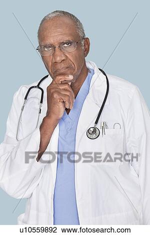 Portrait of a serious African American doctor with hand on chin over light blue background View Large Photo Image Stock Image - Portrait of a serious African American doctor with hand on chin over light blue background. Fotosearch