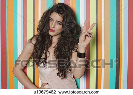 Stock Image - Portrait of a woman gesturing victory sign against colorful striped background. Fotosearch