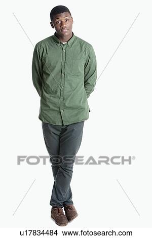 Picture - Portrait of a young African American man standing with legs crossed over gray background. Fotosearch