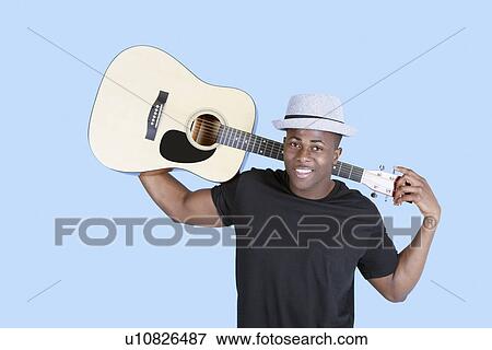 Stock Photo - Portrait of a young African American man carrying guitar over light blue background. Fotosearch