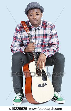 Stock Photograph - Portrait of a young African American man with guitar over light blue background. Fotosearch