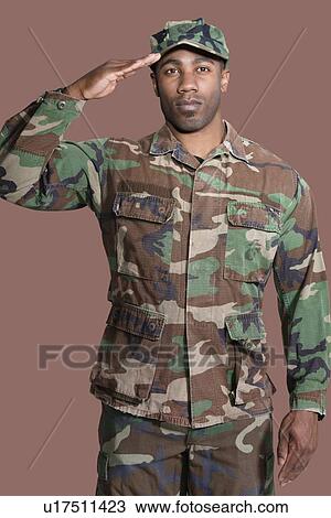 Stock Image - Portrait of a young African American US Marine Corps soldier saluting over brown background. Fotosearch