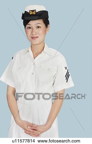Portrait of a young female US Navy officer standing with hands clasped over light blue background View Large Photo Image Picture - Portrait of a young female US Navy officer standing with hands clasped over light blue background. Fotosearch