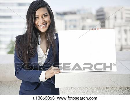 Stock Image - Portrait of a young Indian businesswoman holding Moodboard sign. Fotosearch