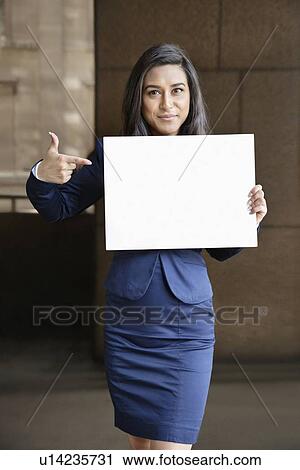 Stock Image - Portrait of a young Indian businesswoman pointing towards Moodboard sign. Fotosearch