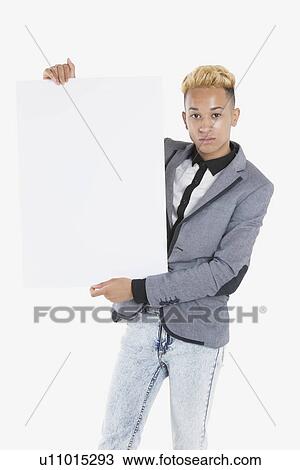 Stock Image - Portrait of a young man holding blank cardboard over gray background. Fotosearch