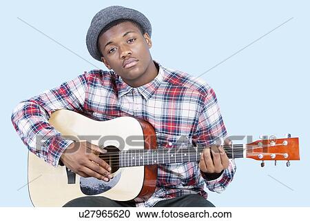 Stock Image - Portrait of a young man playing guitar over light blue background. Fotosearch