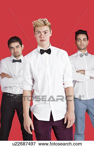 Portrait of a young man standing in front of male friends over red background View Large Photo Image Stock Photo - Portrait of a young man standing in front of male friends over red background. Fotosearch