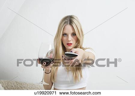 Portrait of a young woman holding wine glass while using remote control View Large Photo Image Stock Image - Portrait of a young woman holding wine glass while using remote control. Fotosearch