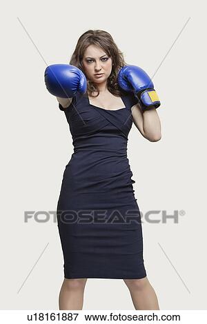 Stock Photo - Portrait of a young woman wearing blue boxing gloves against gray background. Fotosearch
