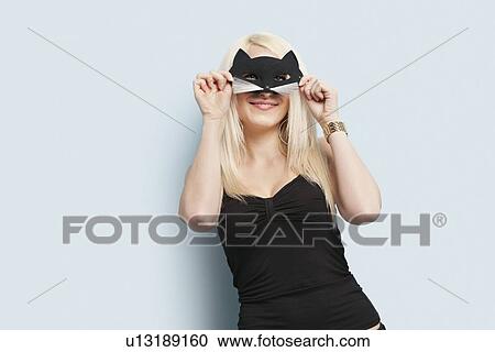 Stock Image - Portrait of a young woman wearing eye mask over light blue background. Fotosearch