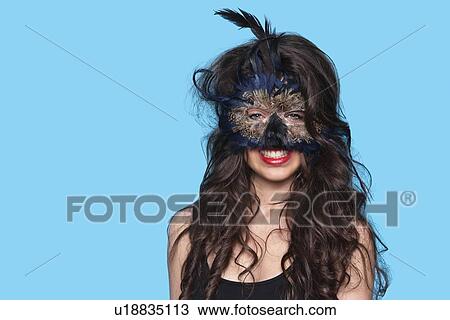 Portrait of a young woman wearing exotic eye mask over blue background View Large Photo Image Stock Image - Portrait of a young woman wearing exotic eye mask over blue background. Fotosearch
