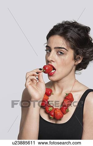 Portrait of a young woman wearing strawberry necklace as she eats one piece over gray background View Large Photo Image Stock Image - Portrait of a young woman wearing strawberry necklace as she eats one piece over gray background. Fotosearch