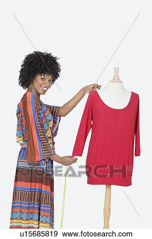 Stock Photo - Portrait of African American female designer measuring a red tunic over gray background. Fotosearch