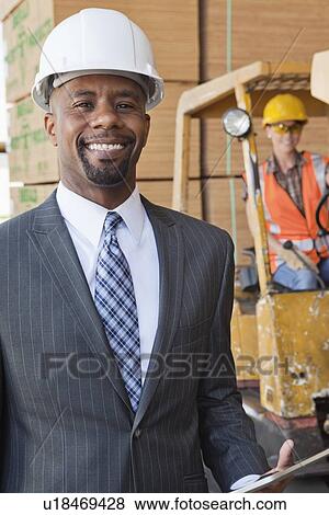 Portrait of African American male engineer smiling with female worker in background View Large Photo Image Stock Photo - Portrait of African American male engineer smiling with female worker in background. Fotosearch