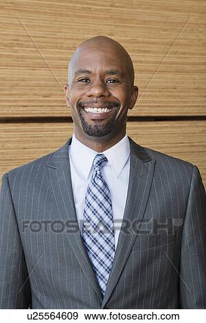 Stock Photo - Portrait of African American businessman smiling with stacked wooden planks in background. Fotosearch