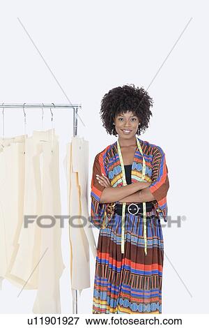 Stock Photo - Portrait of an African American female designer with sewing patterns on clothes rack over gray background. Fotosearch