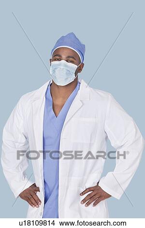 Picture - Portrait of an African American male surgeon with hands on hips over light blue background. Fotosearch