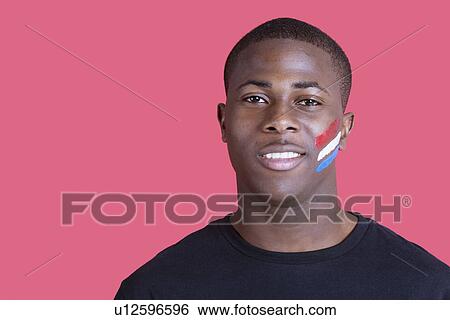 Stock Photograph - Portrait of an African American man with Dutch flag on his face over pink background. Fotosearch