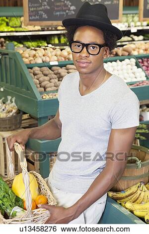 Stock Photograph - Portrait of an African American man with vegetable basket at supermarket. Fotosearch