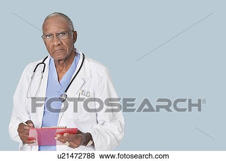 Stock Photo - Portrait of an African American senior doctor holding clipboard over light blue background. Fotosearch