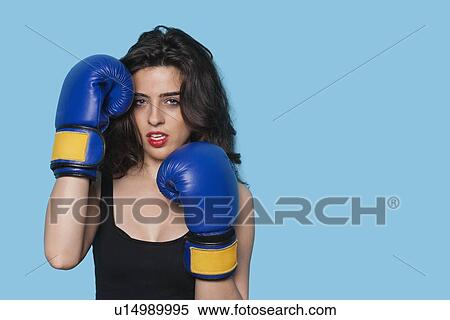Portrait of an aggressive young woman wearing boxing gloves over blue background View Large Photo Image Stock Photography - Portrait of an aggressive young woman wearing boxing gloves over blue background. Fotosearch