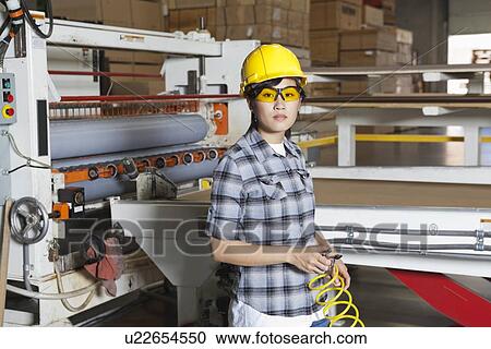 Stock Image - Portrait of an Asian female industrial worker with holding wire with machinery in background. Fotosearch