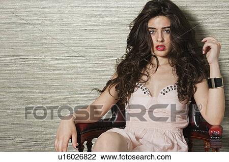 Stock Image - Portrait of an attractive young woman sitting on chair over textured background. Fotosearch