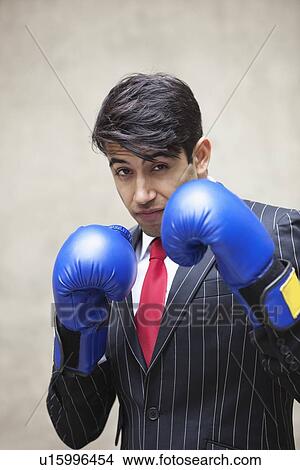 Picture - Portrait of an Indian businessman wearing blue boxing gloves against gray background. Fotosearch