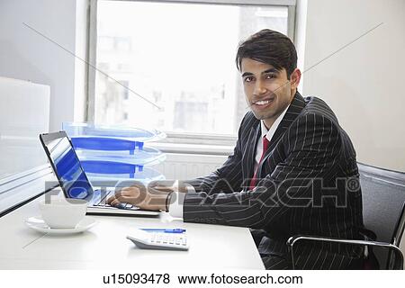 Stock Photo - Portrait of an Indian businessman writing on paper at desk in office. Fotosearch