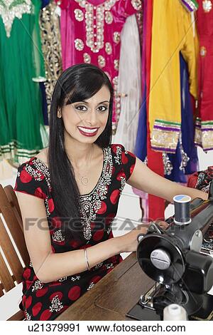 Stock Image - Portrait of an Indian female dressmaker using sewing machine. Fotosearch