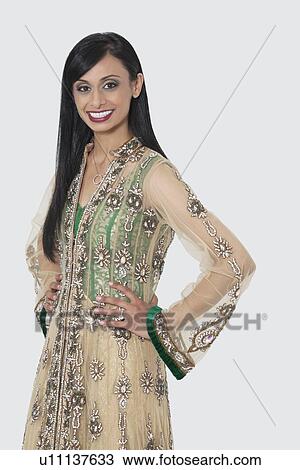 Stock Image - Portrait of an Indian woman in designer wear standing with hands on hips over gray background. Fotosearch