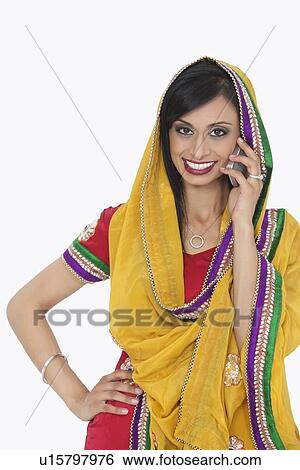 Stock Photograph - Portrait of an Indian woman in traditional wear answering phone call over white background. Fotosearch