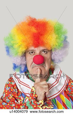 Stock Photo - Portrait of angry senior male clown with finger on chin over light gray background. Fotosearch