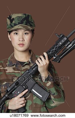 Stock Photo - Portrait of beautiful young US Marine Corps soldier with M4 assault rifle over brown background. Fotosearch