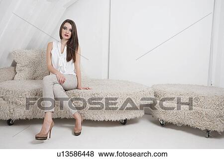 Portrait of beautiful young woman sitting on sofa View Large Photo Image Stock Photo - Portrait of beautiful young woman sitting on sofa. Fotosearch