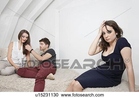 Stock Image - Portrait of bored young woman with couple in background. Fotosearch