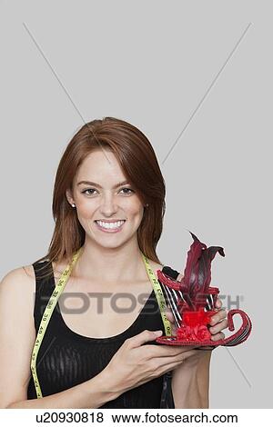 Stock Photo - Portrait of female fashion designer holding stylish hat against colored background. Fotosearch