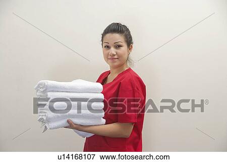 Stock Photo - Portrait of female housekeeper holding clean white towels against gray background. Fotosearch