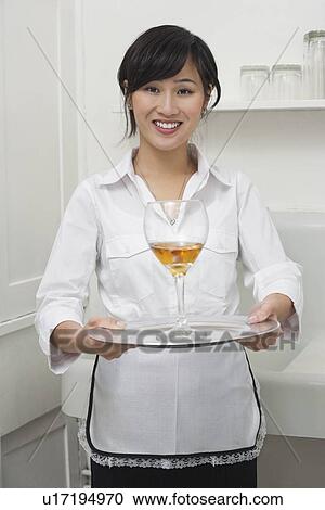 Stock Image - Portrait of female housekeeper serving wine in goblet. Fotosearch