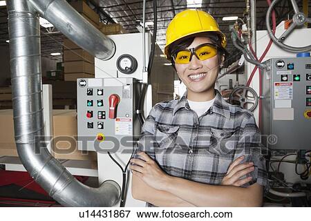 Portrait of female industrial worker smiling while standing in factory with machines in background View Large Photo Image Stock Photo - Portrait of female industrial worker smiling while standing in factory with machines in background. Fotosearch