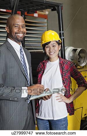 Stock Photo - Portrait of female industrial worker standing with male inspector. Fotosearch