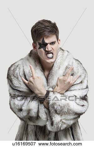 Portrait of frustrated young man in fur coat clenching teeth and making rebellious gesture against gray background View Large Photo Image Stock Photo - Portrait of frustrated young man in fur coat clenching teeth and making rebellious gesture against gray background. Fotosearch