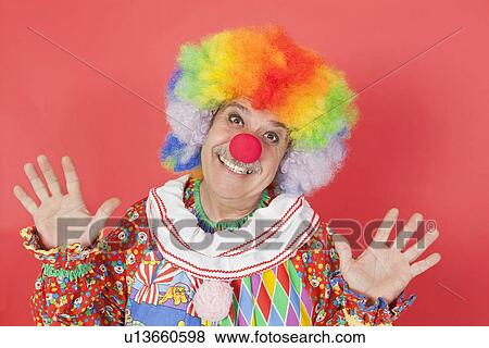 Stock Photo - Portrait of funny clown with arms raised against colored background. Fotosearch
