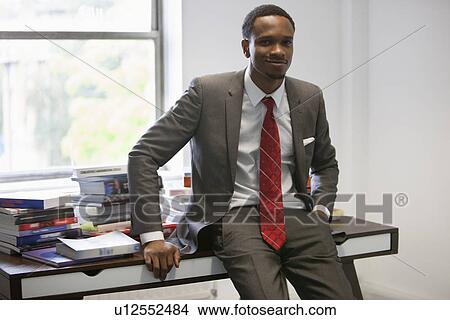 Picture - Portrait of happy African American businessman sitting on office desk. Fotosearch