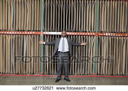 Stock Image - Portrait of happy African American businessman standing arms outstretched in front of thin veneer sheets. Fotosearch