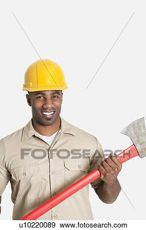 Stock Photo - Portrait of happy African male construction worker holding axe over gray background. Fotosearch