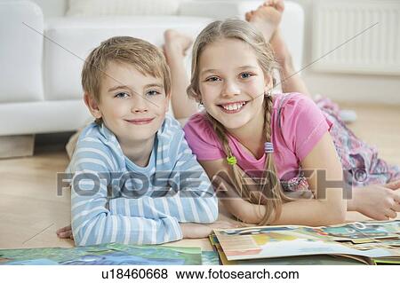 Stock Photo - Portrait of happy brother and sister with story books while lying on floor. Fotosearch