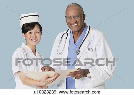 Stock Photo - Portrait of happy health care professionals with medical report over light blue background. Fotosearch