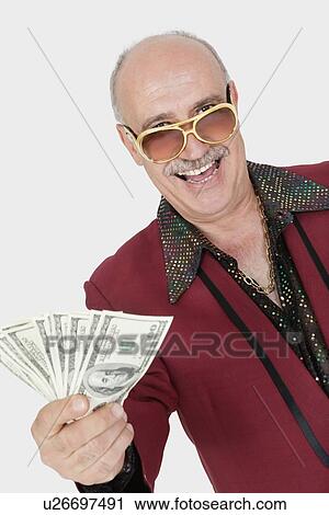 Stock Image - Portrait of happy senior man showing US banknotes against gray background. Fotosearch